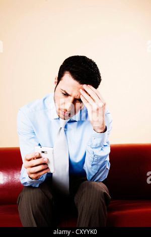 Young manager sitting pensively with his smartphone on a sofa Stock Photo