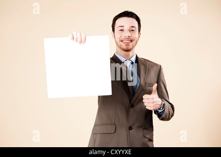 Young man wearing a suit recommending a blank board in his hand with a thumbs-up gesture Stock Photo