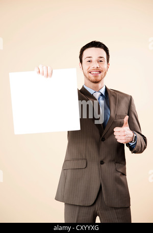 Young man wearing a suit recommending a blank board in his hand with a thumbs-up gesture Stock Photo