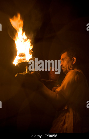 A Hindu Pujari (priest) raises flaming offerings from worshippers at Vishram ghat, Mathura, India Stock Photo