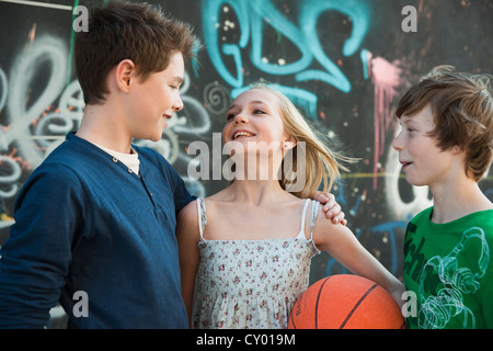 A girl holding a basketball asking two boys to play with her Stock Photo