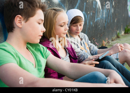 Three teenagers with a tablet PC sitting in front of a wall with graffiti Stock Photo