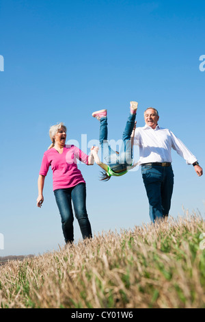 Grandparents swinging their granddaughter in the air with their hands Stock Photo