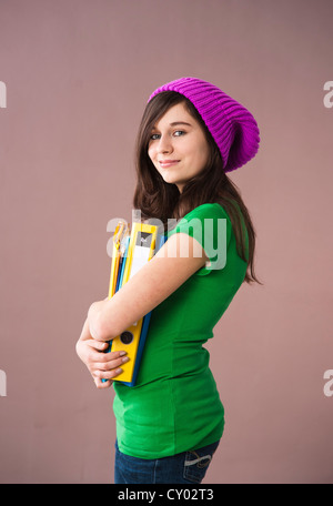 Girl with long hair wearing a hat and holding her school books in her arms Stock Photo