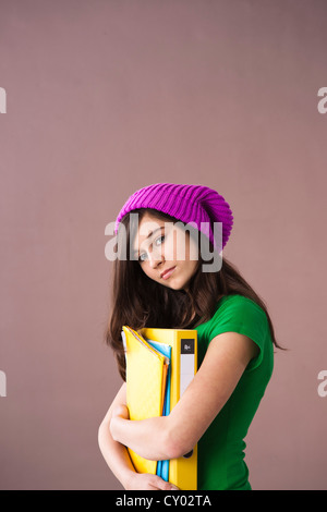 Girl with long hair wearing a hat and holding her school books in her arms Stock Photo