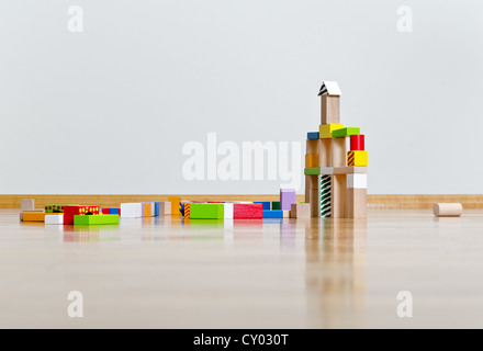 Multicolored building blocks on wooden floor against white wall Stock Photo