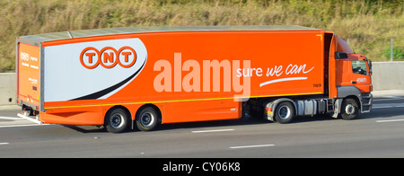 Side view TNT Express freight delivery business hgv supply chain lorry truck & articulated trailer driving along M5 motorway road Essex England UK Stock Photo