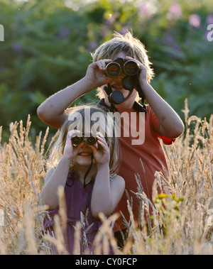 Young boy and girl ) brother and sister) bird watching in meadow in summer Norfolk Model Released Stock Photo