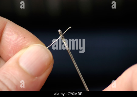 A needle and thread sew up a hole in a denim. Work of a seamstress or  tailor with a needle Stock Photo - Alamy