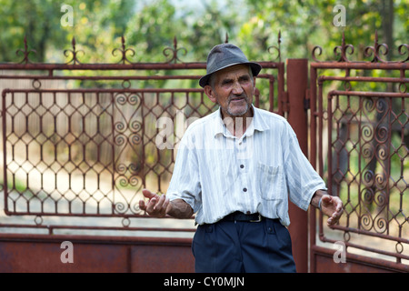 Portrait of an old man standing near a metal gate in the countryside Stock Photo