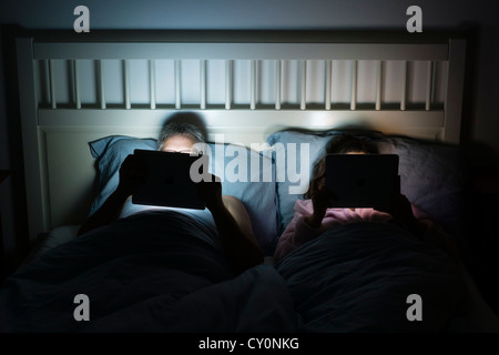 Couple together in bed at night both using iPad tablet computers Stock Photo