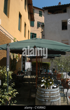 Empty wine bottles sitting on a barrel outside a restaurant with set tables in the background with green sun umbrellas Stock Photo