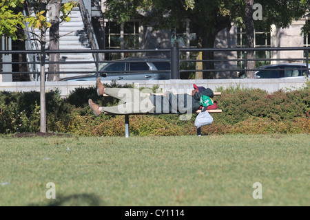 Homeless man sleeping on picnic table one foot up Stock Photo