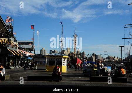 Blue sky view, to Brooklyn, people, water taxi ticket booth, sail ship masts, flags, Pier 17, South Street Seaport, New York Stock Photo