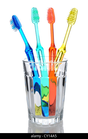 Four multi-colored-toothbrushes standing in a water glass. Vertical format over a white background with reflection. Stock Photo