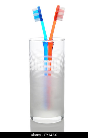 A red and blue toothbrush standing in a frosted water glass. Vertical format on a white background with reflection. Stock Photo