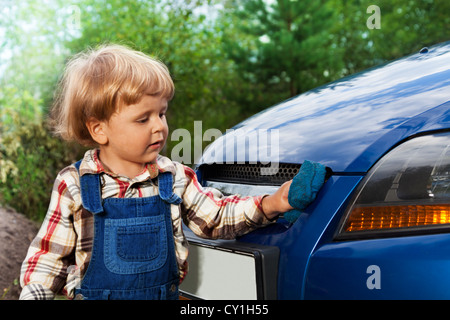 cute little kid in mechanic pants washing blue car with sponge Stock Photo