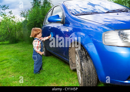 little child washing hatchback car in the countryside Stock Photo