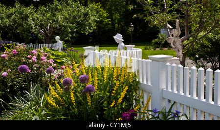 Colorful spring flower garden border, yellow Carolina Lupine, Allium Globe and a white picket fence garden in New Jersey, USA, False Indigo Baptisia Stock Photo