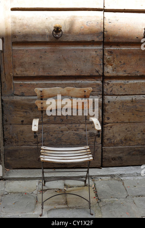 Rustic wood and metal chair in front of an old door in Montecatini Alto Tuscany Italy Stock Photo