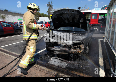 A fireman pictured putting out a car which caught fire in the heat in ASDA car park in Brighton, East Sussex, UK. Stock Photo