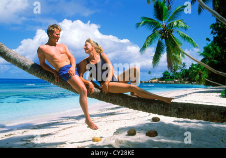 Couple relaxing on palm tree trunk over Anse Severe beach on La Digue Island in Seychelles Stock Photo