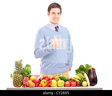 Smiling guy holding a glass of water behind a table full of healthy food isolated on white background Stock Photo