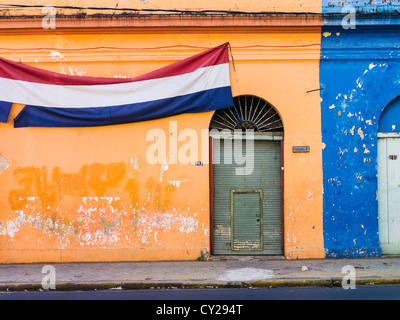A banner representing the colors of the flag of Paraguay is draped across a colorful orange and blue wall in Asunción. Stock Photo