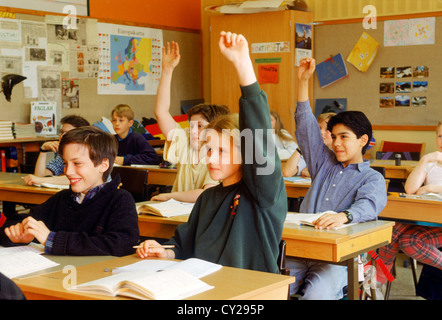 Elementary school children sitting at individual desks in Swedish classroom raising hands to answer questions Stock Photo