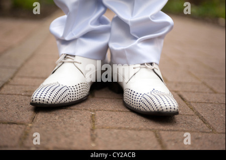 A closeup of a bridegrooms feet in white shoes stood on a pavement Stock Photo