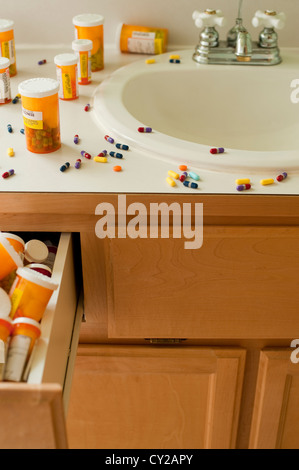 Pills and pill bottles scattered over sink counter in bathroom with drawer stuffed with pill bottles Stock Photo