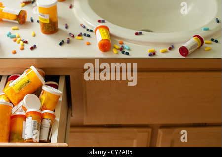 Pills and pill bottles scattered over sink counter in bathroom with drawer stuffed with pill bottles Stock Photo