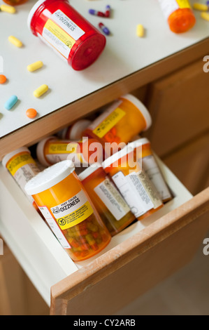 Pills and pill bottles scattered over sink counter in bathroom with drawer stuffed with pill bottles Stock Photo