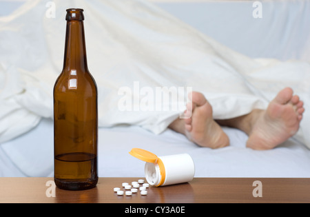 Beer bottle and pills on the table. Person sleeping in the background. Stock Photo