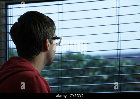 Young male wearing glasses, sitting looking out of a window. Stock Photo