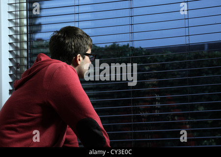 Young male wearing glasses, sitting looking out of a window -evening/night . Stock Photo