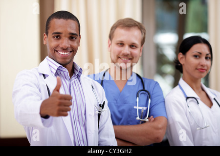 Smiling african-american doctor making thumbs up sign with colleagues standing behind Stock Photo