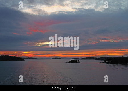 Sunset in cloudy sky over the sea and the wake of a ship between the islands Stock Photo