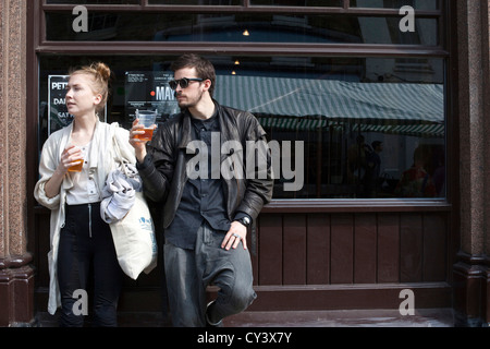 A couple stand and drink outside the Cat and Mutton pub in Broadway Market, London Fields, Hackney, East London Stock Photo