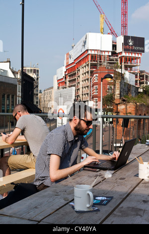 A young man works at his laptop computer on the roof of the Boxpark - a 'pop up mall' comprising of old shipping containers, Stock Photo