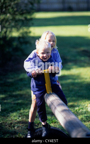 Young children, boy aged 2.5 and girl aged 5 on sea saw together. Stock Photo