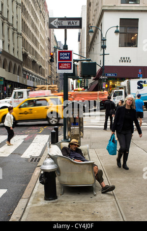 A man is sleeping on a couch on a busy Manhattan sidewalk. Stock Photo