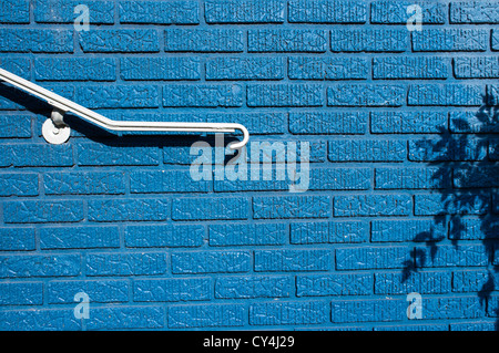 A white railing and shadows contrast against a brightly painted blue brick wall. Stock Photo