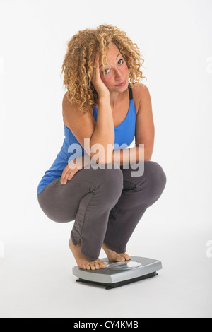 Portrait of young woman crouching on weight scale, studio shot Stock Photo