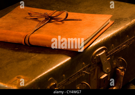 old, vintage, antique leather suitcase with leather bound and tied book on top painted with warm light Stock Photo