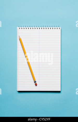 Single yellow sharpened pencil with blank stenographer notebook on blue background Stock Photo