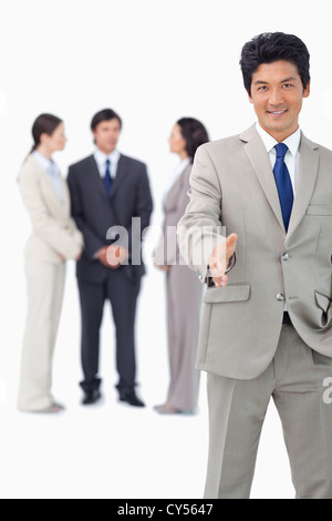 Businessman with colleagues behind him extending his hand Stock Photo