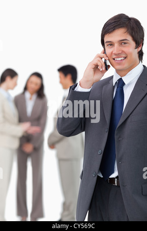 Smiling salesman on his cellphone with team behind him against a white ...