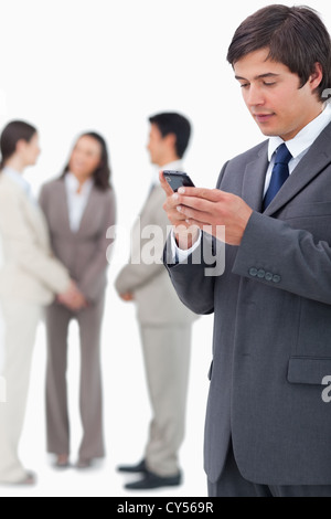 Salesman reading text message on cellphone with team behind him Stock Photo