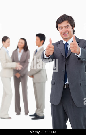 Salesman giving thumbs up with team behind him Stock Photo